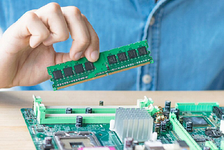 A photo of a man’s hand installing a memory module in a computer’s printed circuit board.