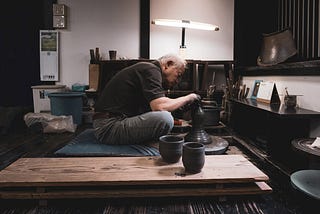 A master Japanese potter makes clay cups at his wheel.