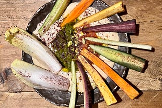 A bowl of hummus and various sticks of vegetables fanned out on top.