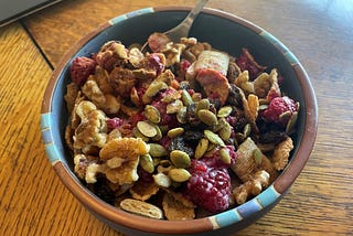A bowl of whole-grain cereal topped with berries, walnuts, raisins, pumpkin seeds, and cinnamon.