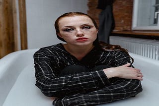 An image depicting a woman sitting in a white bathtub, wearing a black and white plaid shirt, her expression conveying a mix of confusion, frustration, and vulnerability, reflecting the impact of identity theft and online insecurity.