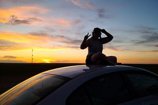 Anne sitting on the roof of her car at sunset