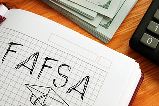 FAFSA drawn on notebook paper with sketch of graduation hat. Stack of money and calculator shown.