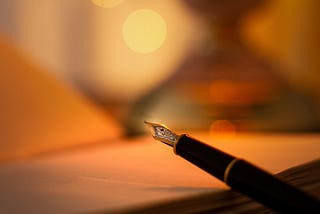 A close-up of a fountain pen resting on an open notebook, softly lit by warm, golden light with a blurred background, evoking a calm and reflective writing atmosphere.