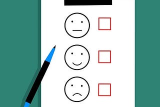 A survey sheet with three facial expressions — neutral, happy, and sad — next to empty checkboxes, with a blue pen placed beside it.