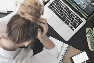 Young woman frustrated in front of a laptop computer. Holding her head in her hands