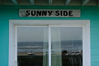 beach reflected in sliding glass door with “sunny side” above the door
