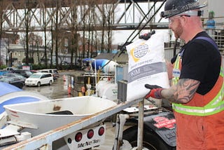 A construction worker is holding a bag of KIM and getting ready to throw it into the ready-mix truck.