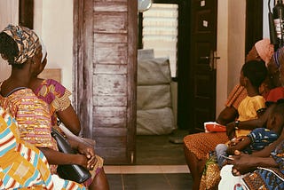Patients in the waiting hall of Atwereboana CHPS compound, Ghana, sit in front of an open door