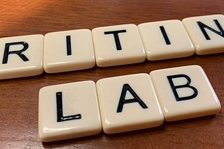 Tile letters from the game “Bananagrams” spell out the words “Writing Lab” on an oak desktop.