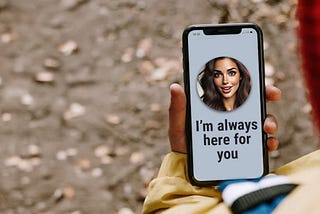A person is holding a phone. On the screen is an AI generated image of a young woman’s face, with the text message “I’m always here for you.”