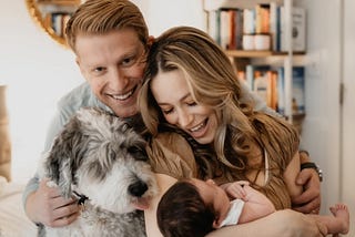 A smiling family with a father, mother, baby, and dog