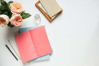 A few sketchbooks rest beside a vase filled with flowers.