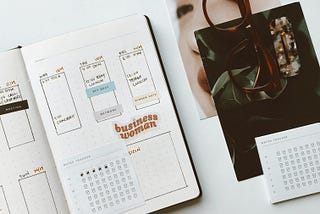 Image of an open planner, calendar, glasses & workspace.