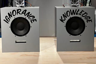 Two speakers on a wood finish table. The one on the left says “ignorance.” The one on the right says “knowledge.” Photo by author, from Virgil Abloh exhibit at The Brooklyn Museum.