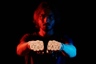 A man with fists pointing forward to the camera and the words “stop hate” written across his fingers