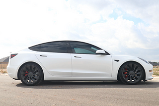 a white Tesla model 3 parked with a blue cloudy sky in the background