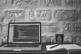 A black-and-white image of a laptop on a desk with a code editor open.