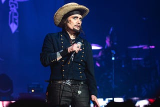 Adam ant on stage in a vaguely military uniform and a straw hat.