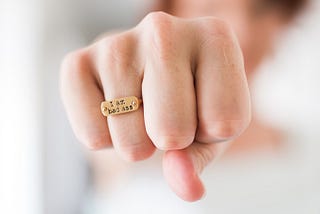 Photo of a fist wearing a ring that says, “I am badass.”