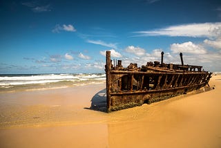 A wrecked boat disgarded on a sandy beach.