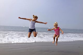 Two extremely joyful little girls, mid-air while jumping simultaneously on the beach.