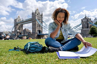 一個女子坐在草皮上讀書，後方是倫敦著名景點