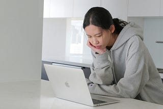 Young, Asian woman staring at a laptop in a minimalist kitchen.