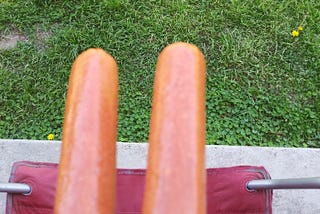A terrible overhead photo of two hot dogs imitating a pair of legs in a camping chair.
