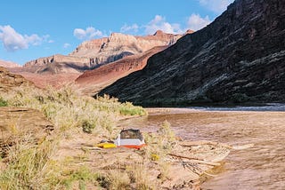 A camping tent set up on the banks of the Colorado River in the Grand Canyon, with the rim of the canyon visible in the distance