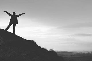 Woman standing on a hillside withher arms outstretched to meet the sunrise