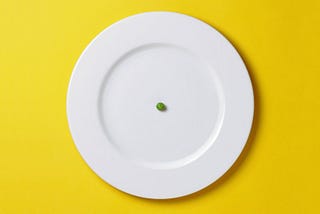 A white plate with a single green pea in the middle