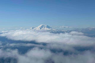 Snow-covered mountain peak of Mount Rainier rising above the clouds