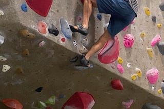 The author taking on a V3–4 boulder problem at a climbing gym. Here I am climbing up a wall with broad holds.