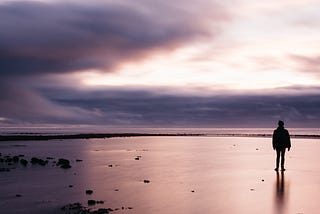 A person on a beach at low tide with clouds on the horizon and on the left