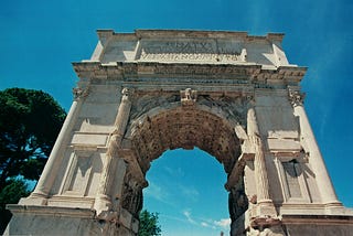 Photo looking up at the Arch of Titus in Rome against a blue sky