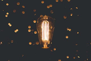 Old fashioned light bulb, with flecks of diffuse gold light on a black background.