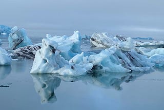 Very icy blue ice bergs floating in a foggy Iceland lagoon, with a beautiful mirror image of the icebergs in the water line.