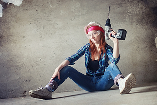 Girl sitting on a concrete floor wearing goggles and holding a drill