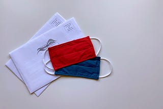 Two “Election Mail” envelopes stacked iwth a red mask and a blue mask laid on top