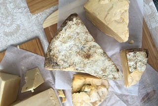 Several ugly-looking wedges of cheese rest on cutting boards on a wooden table