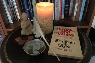 A candle, Buddha figurine, runes, a feather and a book on grammar sit on a table