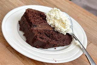 Devil’s Food Chocolate Cake, on white plate, with a spoon with whipped cream on it