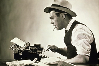 b&w photo of old fashioned jounralist at a typewriter wearing a hat smiking.