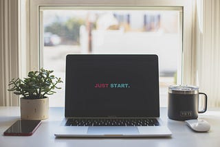 laptop on desk with words “Just start” on screen, succulent on the left, coffee mug to the right