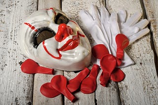 Clowns mask with white gloves and red balloons on wooden boards