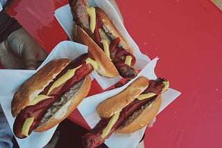 Three hot dogs on buns, held with white paper over a red background