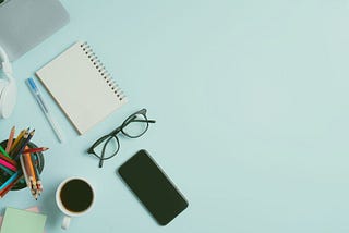 A notebook, smartphone, pencils, headphones, glasses, and a cup of coffee.