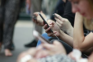 Group of people waiting for the train and looking down, scrolling on their smartphones.