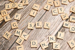 Scattered Scrabble tiles on a table. In the centre of the picture, slightly separate from the other tiles, are the letters S, E, and X.